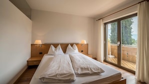 A hotel room with a large bed, wooden headboard, two bedside lamps, a sliding glass door to a balcony, and a view of trees. - Apartment "Weinsepphof 3" with Mountain View, Pool, Wi-Fi, Garden & Balcony (Lana)
