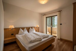 A bedroom with a wooden bed, two bedside lamps, a sliding glass door to a balcony, and a ceiling light.