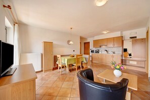Une cuisine moderne avec des meubles en bois, un coin repas avec une table et des chaises, un téléviseur posé sur un meuble, et un vase rempli de fleurs sur une table.