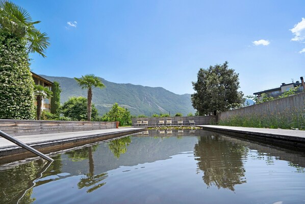 Une piscine avec une terrasse en bois, des chaises et une vue sur les montagnes en arrière-plan.