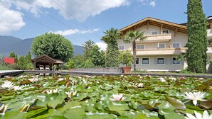 Un hotel con piscina rodeado de nenúfares, una terraza de madera y montañas al fondo.