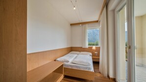 Un dormitorio con cama de madera, una mesita de noche, una ventana con vistas a montañas y una puerta corredera de vidrio que da a un espacio exterior.