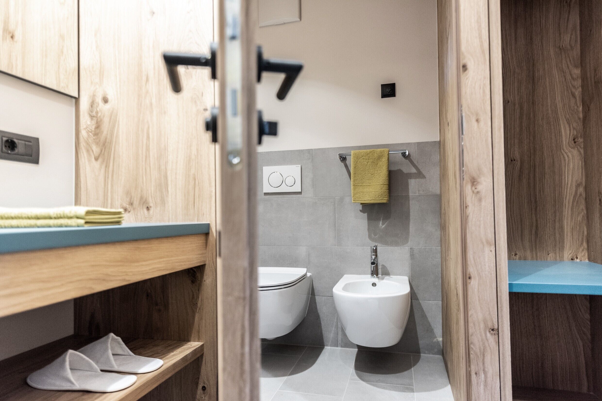 Une salle de bain moderne avec un meuble-lavabo en bois, des toilettes, un bidet et un porte-serviettes.