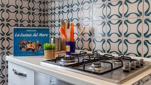 A kitchen with a gas stove, a book titled 'La Cucina del Mare,' and a decorative backsplash. - Apartment San Giovanni Lido Close to the Beach with Sea View & Balcony (Alghero)