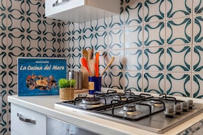 A kitchen with a gas stove, a book titled 'La Cucina del Mare,' and a decorative backsplash. - Apartment San Giovanni Lido Close to the Beach with Sea View & Balcony (Alghero)