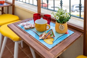 A table with a placemat, a yellow mug, red cups, a vase with flowers, and a small card.