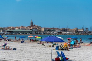 Une plage avec des parasols, des gens qui prennent un bain de soleil et, au loin, un bâtiment surmonté d’une tour.