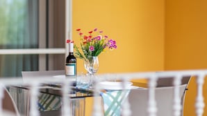 A dining table with a bottle of wine, a glass vase with flowers, and a window with blinds in the background. - Villa Casa Angus with partial Sea View, A/C, Garden & Terrace; Pet-friendly (BADESI)