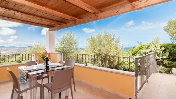 A wooden balcony with a table set for two, overlooking a scenic landscape with trees and a view of the sea. - Villa Casa Angus with partial Sea View, A/C, Garden & Terrace; Pet-friendly (BADESI)