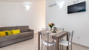 A living room with a sofa, dining table, chairs, a flat-screen TV, and an air conditioning unit. - Villa Casa Angus with partial Sea View, A/C, Garden & Terrace; Pet-friendly (BADESI)
