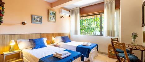 A hotel room with two beds, a small table, a chair, and a window with curtains.
