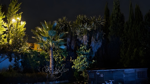 Una piscina con borde iluminado en azul, rodeada de césped y árboles.