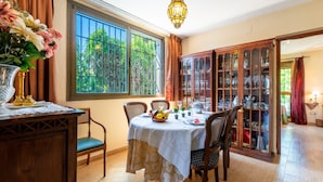 Comedor con una mesa preparada para cuatro, una vitrina con puertas de cristal y un gran ventanal con cortinas.