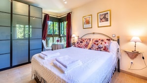 Un dormitorio con cama, mesita de noche, estante en la pared y ventana con cortinas.