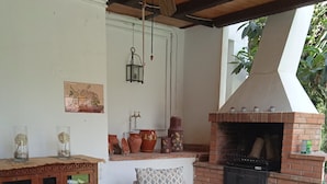 Un patio al aire libre con mobiliario de mimbre, un horno de ladrillo y macetas decorativas.