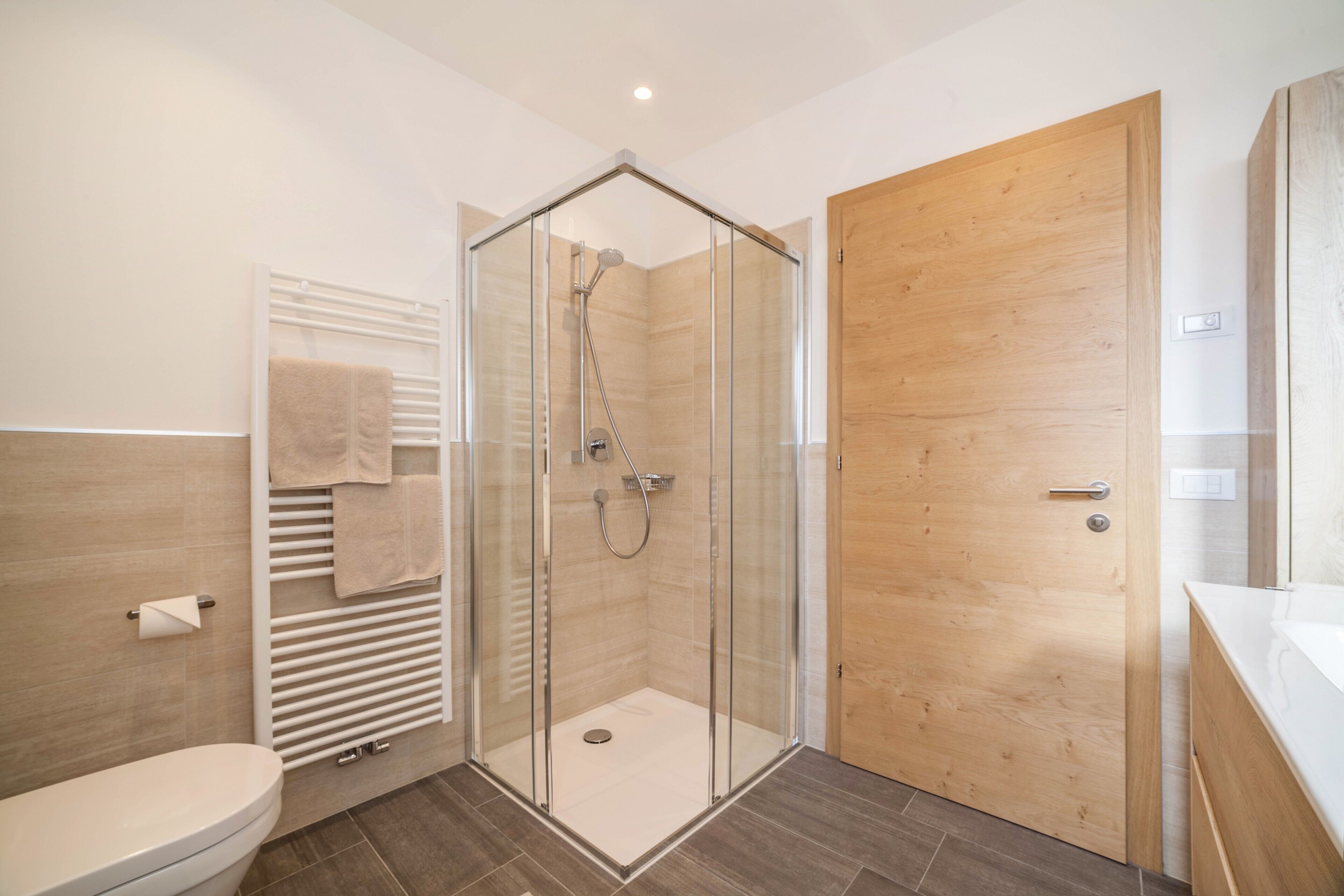 Un bagno moderno con doccia vetrata, porta in legno, WC bianco e portasci.