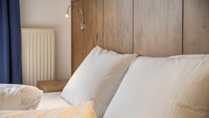 Et soveværelse med sengegavl i træ, hvide sengetæpper, et natbord og en vægmonteret lampe.