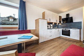 A modern kitchen with a dining area, wooden cabinets, a built-in oven, and a large window with a view of a house. - Holiday Apartment "Residenz Condor Rosengarten" with Mountain View, Sauna, Wi-Fi & Garden (Meransen)