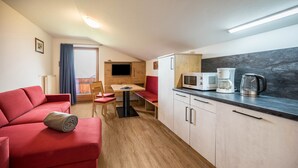 A compact living space with a red sofa, a dining area, a kitchenette with a microwave, coffee maker, and cabinets. - Holiday Apartment "Residenz Condor Schlern" with Mountain View, Sauna & Garden (Meransen)