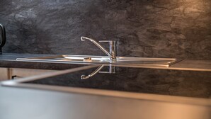 A modern kitchen with a stainless steel faucet, a reflective backsplash, and a sleek countertop. - Holiday Apartment "Residenz Condor Schlern" with Mountain View, Sauna & Garden (Meransen)