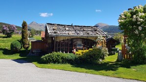 A rustic wooden building with a sloped roof, surrounded by well-maintained greenery and a clear view of mountains in the background. - Holiday Apartment "Residenz Condor Schlern" with Mountain View, Sauna & Garden (Meransen)