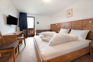 Ein Schlafzimmer mit einem hölzernen Bett, einem Schreibtisch, einem Sessel, einem Fernseher und einem Fenster mit Vorhängen.