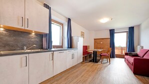 Una cucina moderna con forno integrato, un'area pranzo con tavolo e sedie, e un divano rosso nella zona living.