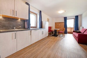 Una cocina moderna con horno empotrado, una zona de comedor con mesa y sillas, y un sofá rojo en la sala de estar.