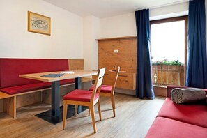 Une pièce avec une table en bois, deux chaises, un canapé rouge, un meuble en bois et une fenêtre avec des rideaux.