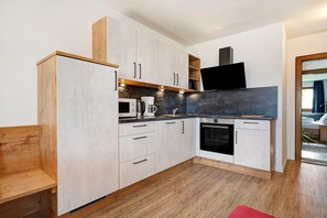 Eine moderne Küche mit Holzschränken, einem Einbauofen und einem Flachbildfernseher.