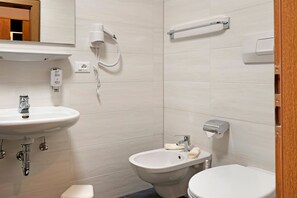 Une salle de bain équipée d’un lavabo, d’un bidet, de toilettes et d’un distributeur de serviettes.