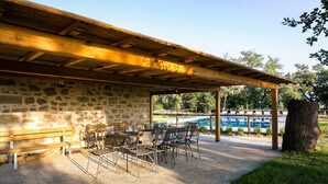 Une terrasse extérieure avec un mur en pierre, une pergola en bois et une piscine en arrière-plan.