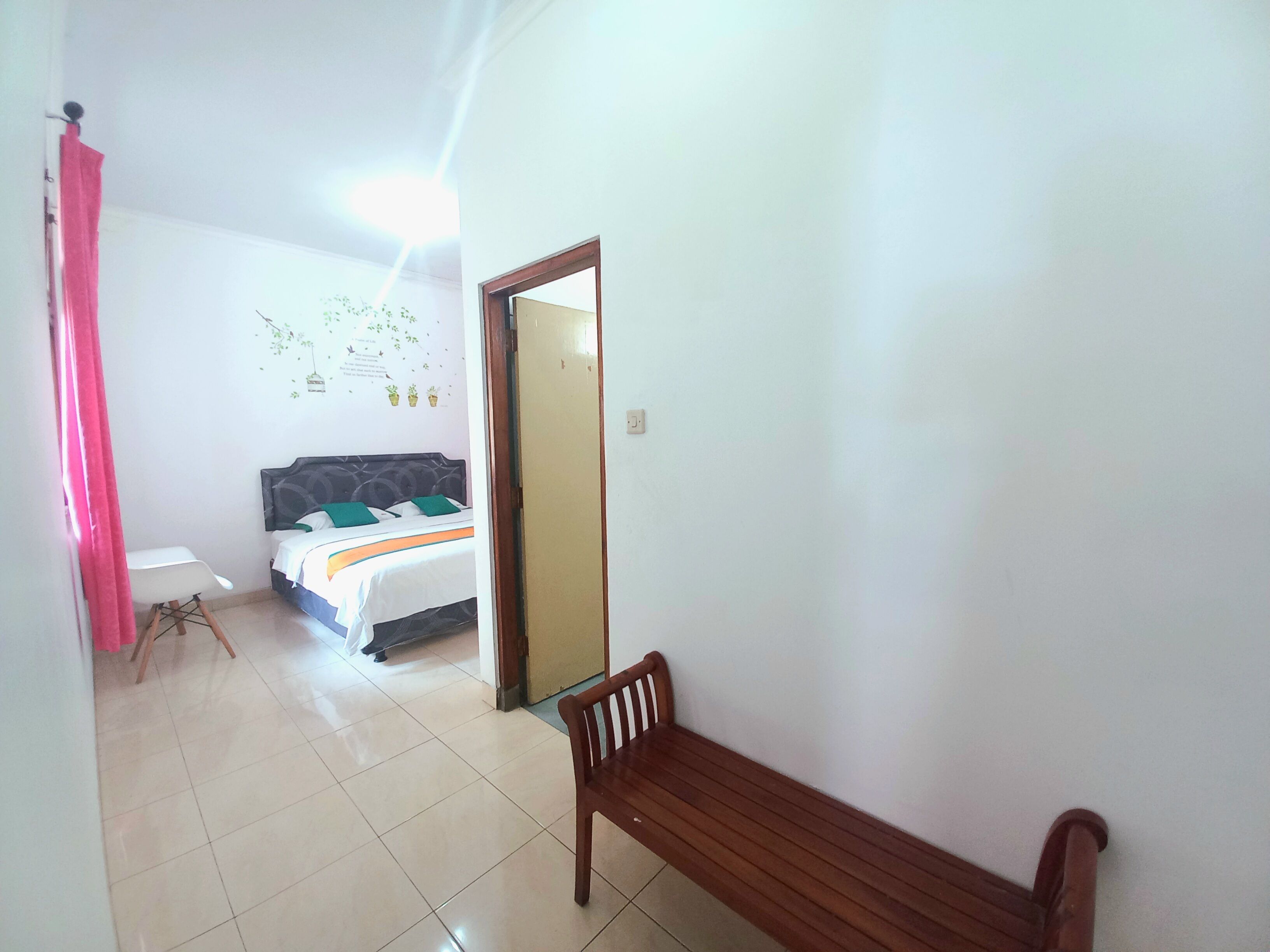 Una habitación de hotel con una cama, un banco de madera, una silla blanca y una cortina rosa.