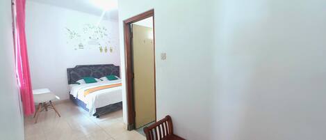 Una habitación de hotel con una cama, un banco de madera, una silla blanca y una cortina rosa.