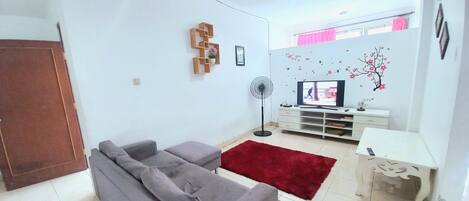 A living room with a grey sofa, a red rug, a TV, and a white cabinet.
