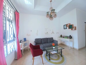 A living room with a grey sofa, a red chair, a glass coffee table, and a chandelier. - Homestay Jogja 4 Kamar Tidur Full AC Seputaran Umbulharjo dekat Gembiraloka (Yogyakarta)