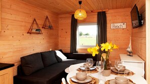 A cozy cabin interior with a black sofa, a dining table set for four, and a window with curtains.