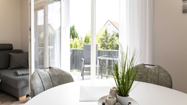 Een moderne woonkamer met een witte tafel, een grijze bank en uitzicht op buiten.