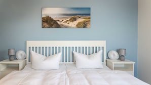 Een slaapkamer met een groot bed, twee nachtkastjes, een aan de muur hangend schilderij van een strand en een blauwe wand.
