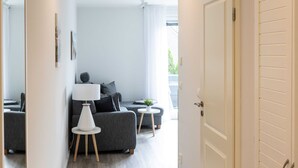 Een moderne woonkamer met een grijze bank, een witte lamp en een klein rond tafeltje met een plant.