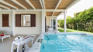 Uma área de piscina com banheira de hidromassagem, uma mesa com garrafas e copos, e vista para o jardim.
