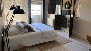 Un dormitorio con cama, lámpara de pie, vistas al exterior y una puerta corredera que da al baño.