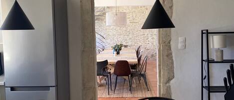 A modern kitchen with a large island, pendant lights, and a view into a dining area with a rustic stone wall.