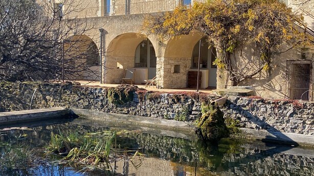 Un edificio de piedra con ventanas arqueadas y un patio que tiene un estanque con lirios.