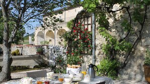 Mesa de comedor al aire libre con desayunos, rodeada de muros de piedra y follaje.