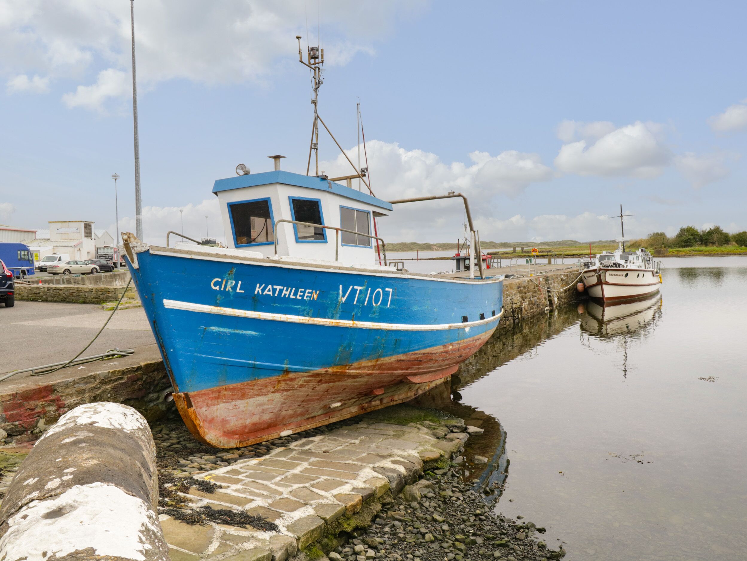 A blue boat named 'Girl Kathleen VT107' docked at a pier.
