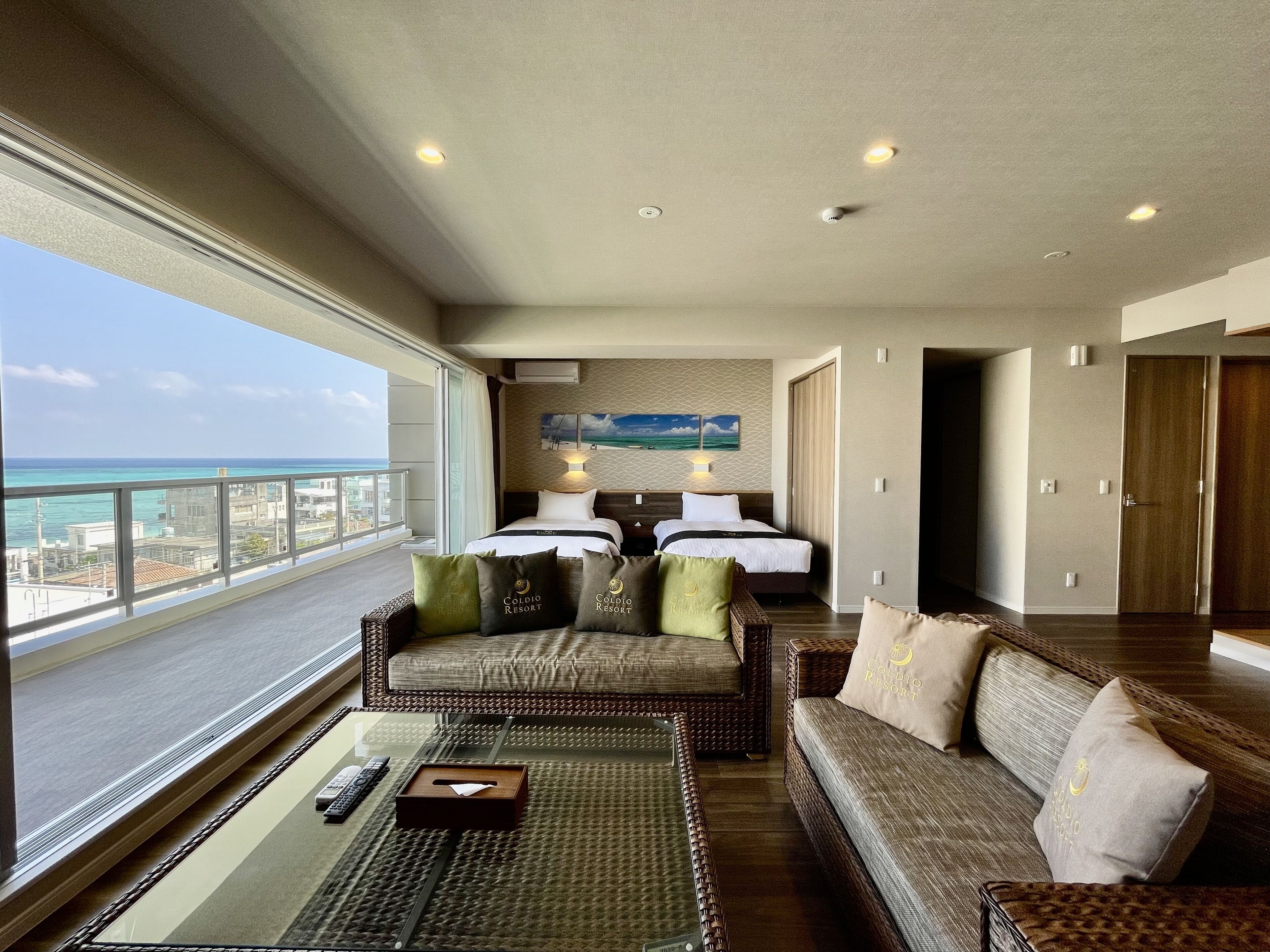 A spacious room with a balcony, a bed with two pillows, a sofa, and a coffee table.