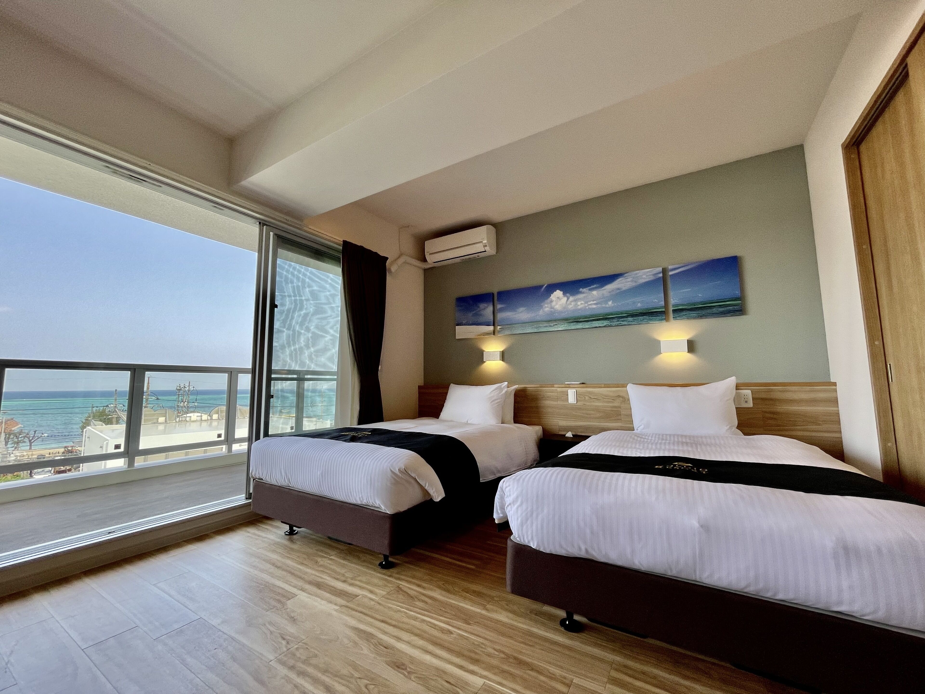 A hotel room with two beds, a large window with a view of the ocean, and a painting on the wall.