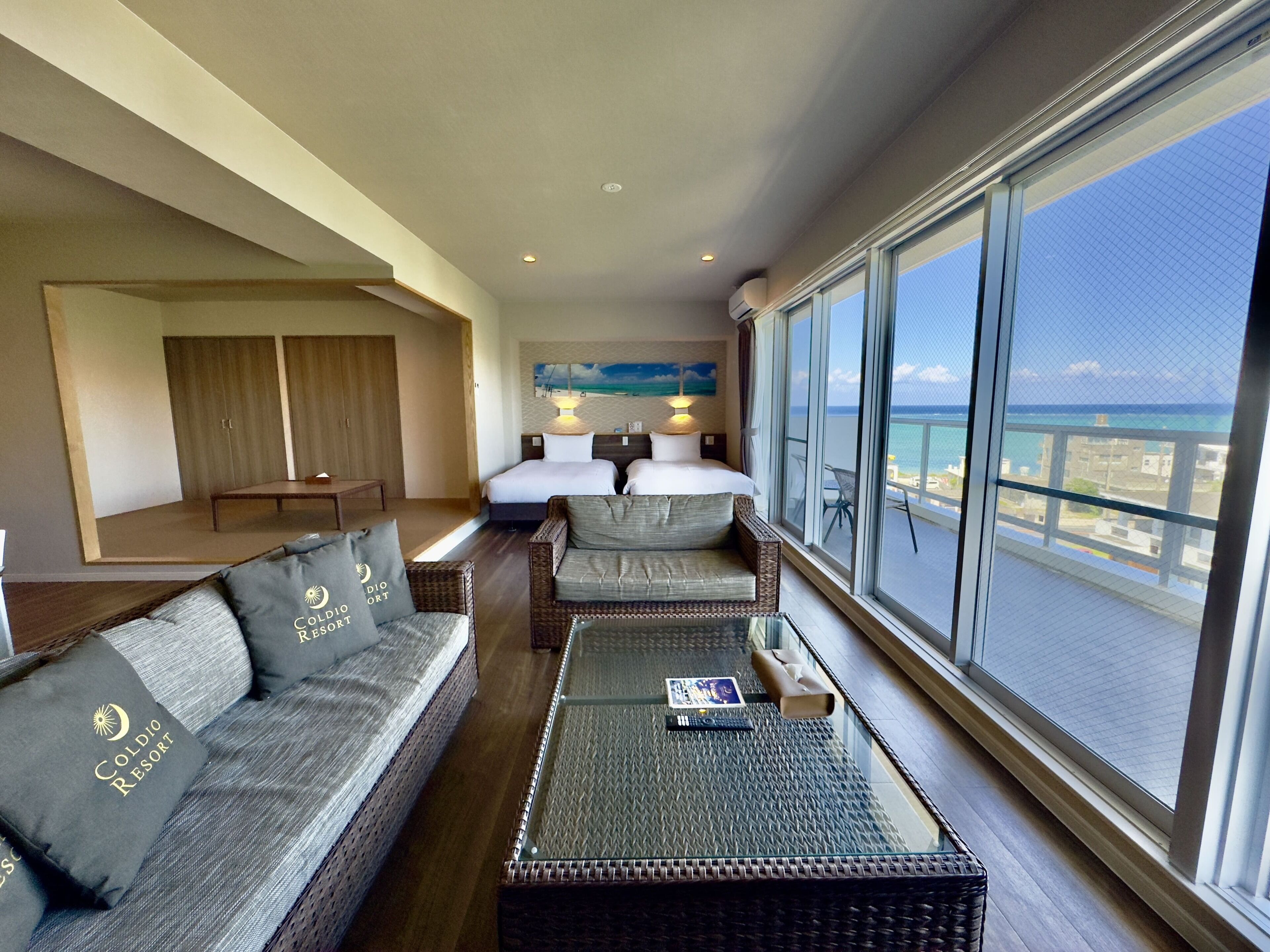 A hotel room with a balcony, a sofa set, a bed, and a view of the ocean.