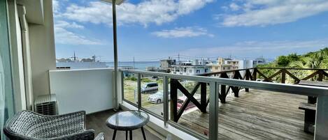 A balcony with wicker furniture, a view of the sea, and a wooden deck.